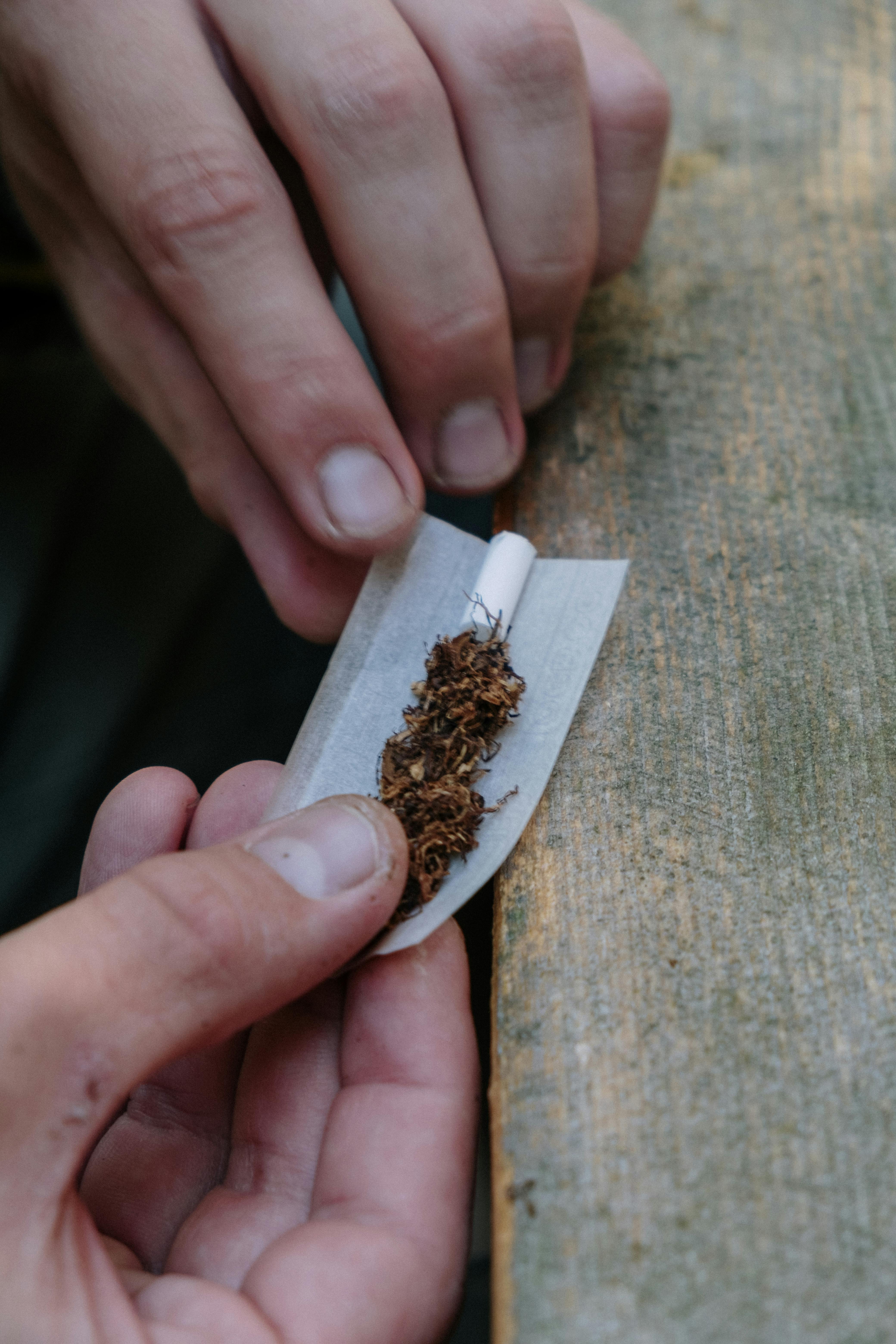 Zeigt Hände, die eine Zigarette mit losem Tabak drehen.